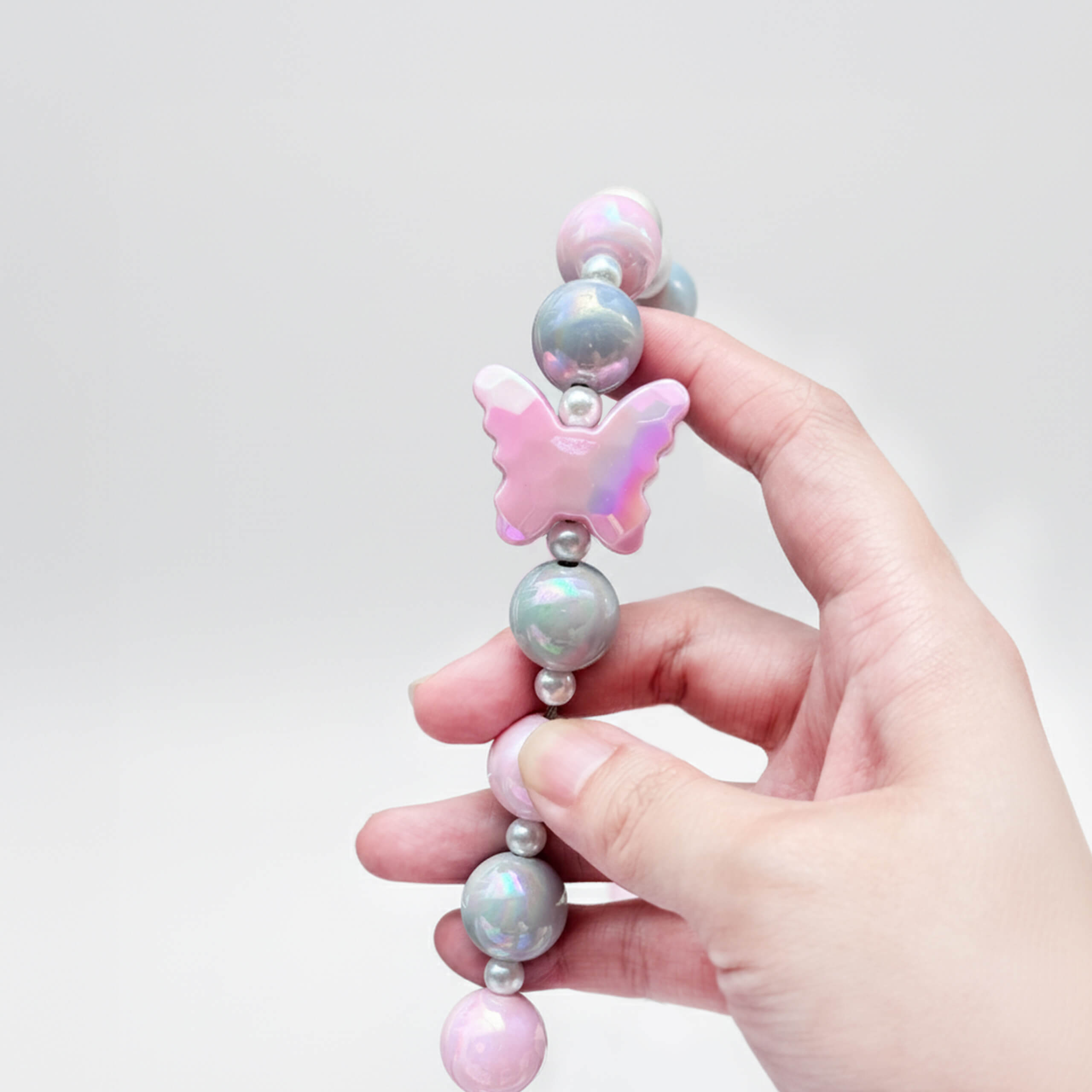 Close-up of JOGIA butterfly charm and beads held in hand, showing pink and gray tones.