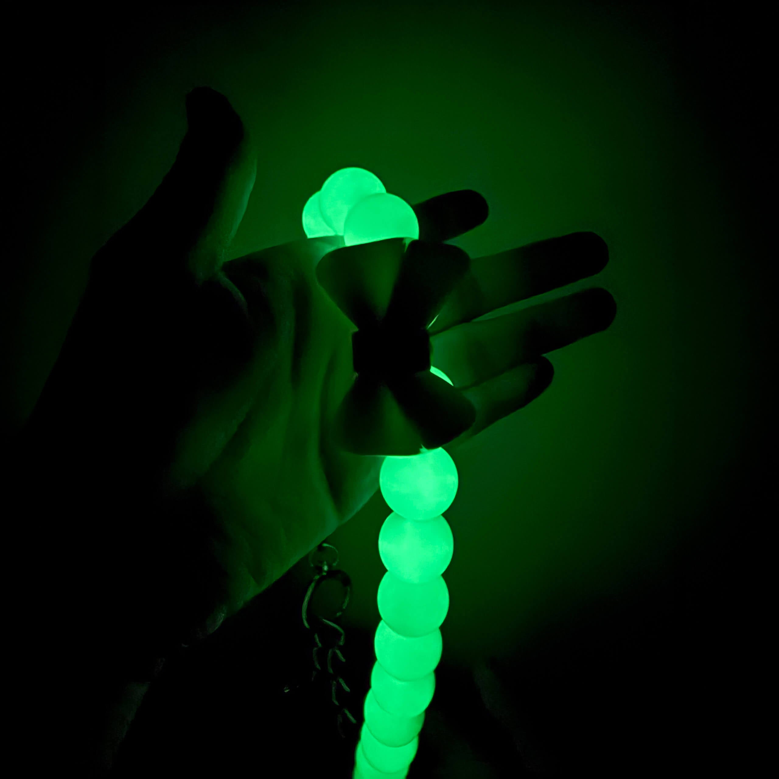 Hand holding JOGIA glow-in-the-dark beads illuminated in the dark.
