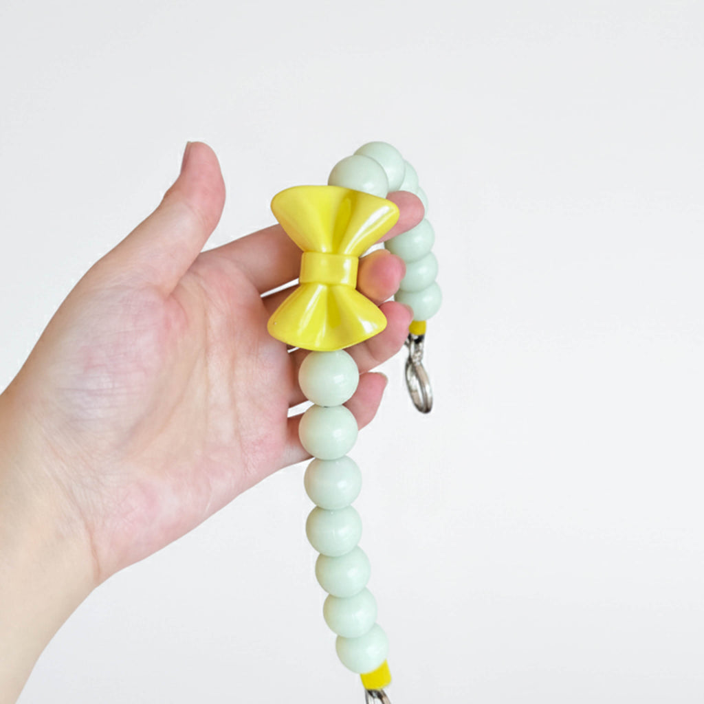 Close-up of JOGIA glow beads and yellow bow charm held in hand, showing the pale green finish.