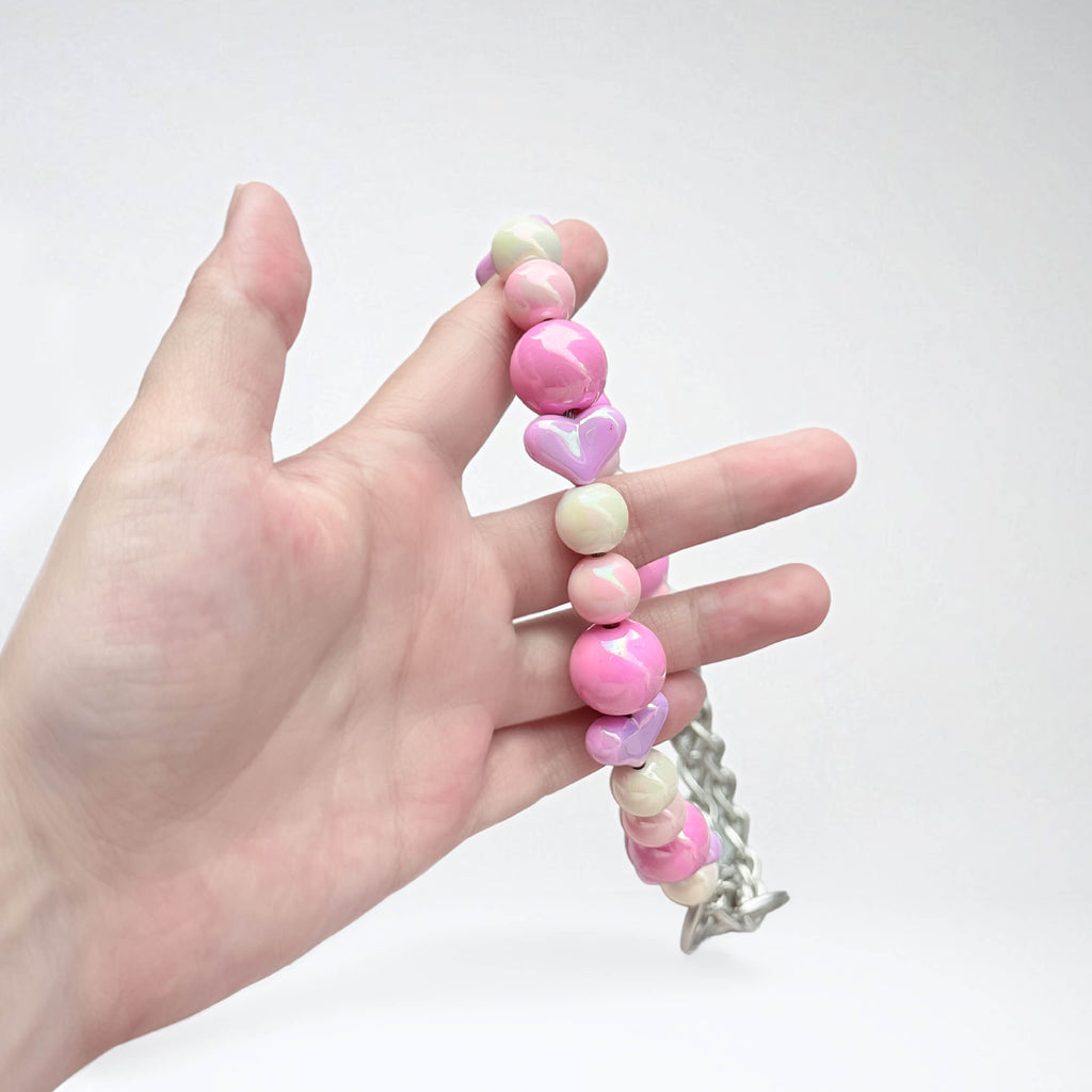 Close-up of JOGIA pink beaded dog collar held in hand, showing heart beads.