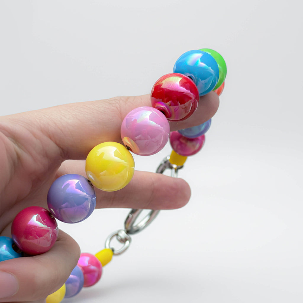 Close-up of JOGIA rainbow beads held in hand, showing glossy multicolor finish.