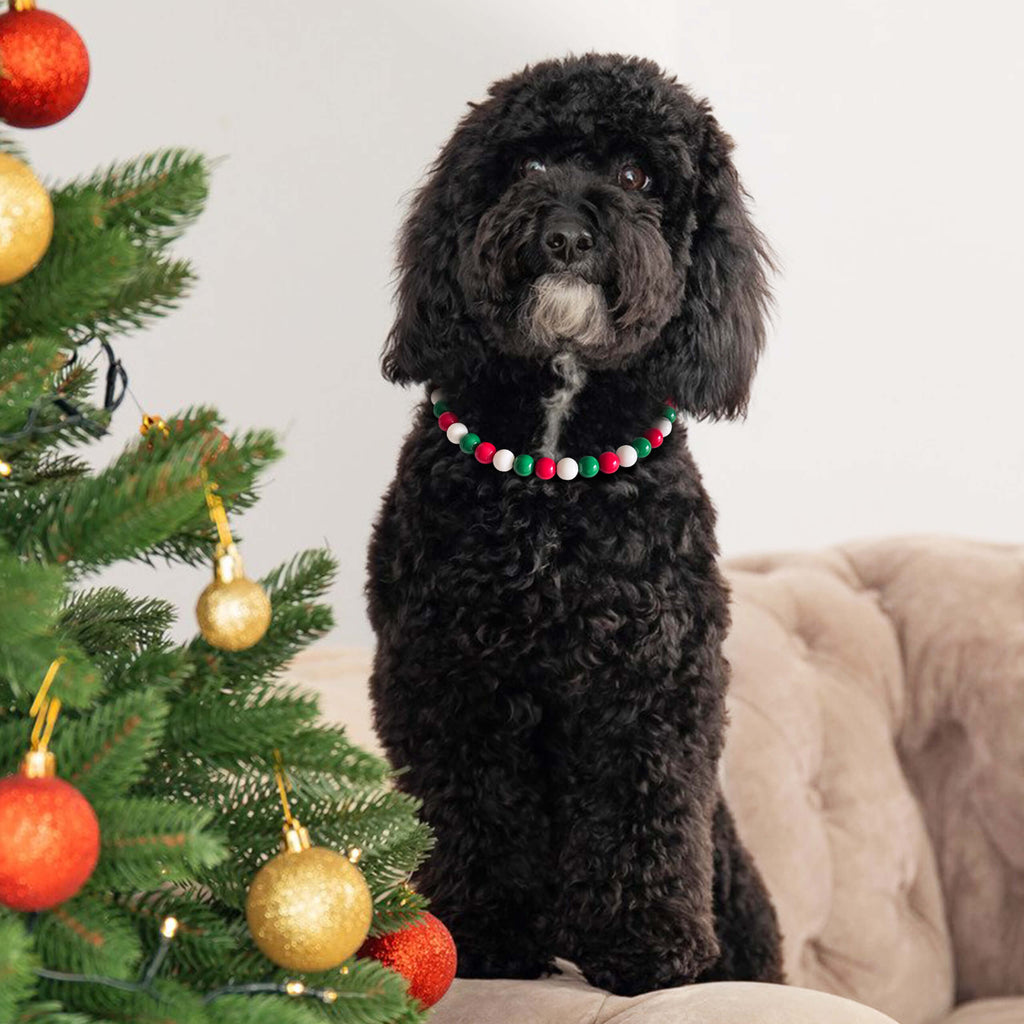 Dog wearing JOGIA Christmas beaded collar sitting beside a decorated Christmas tree.